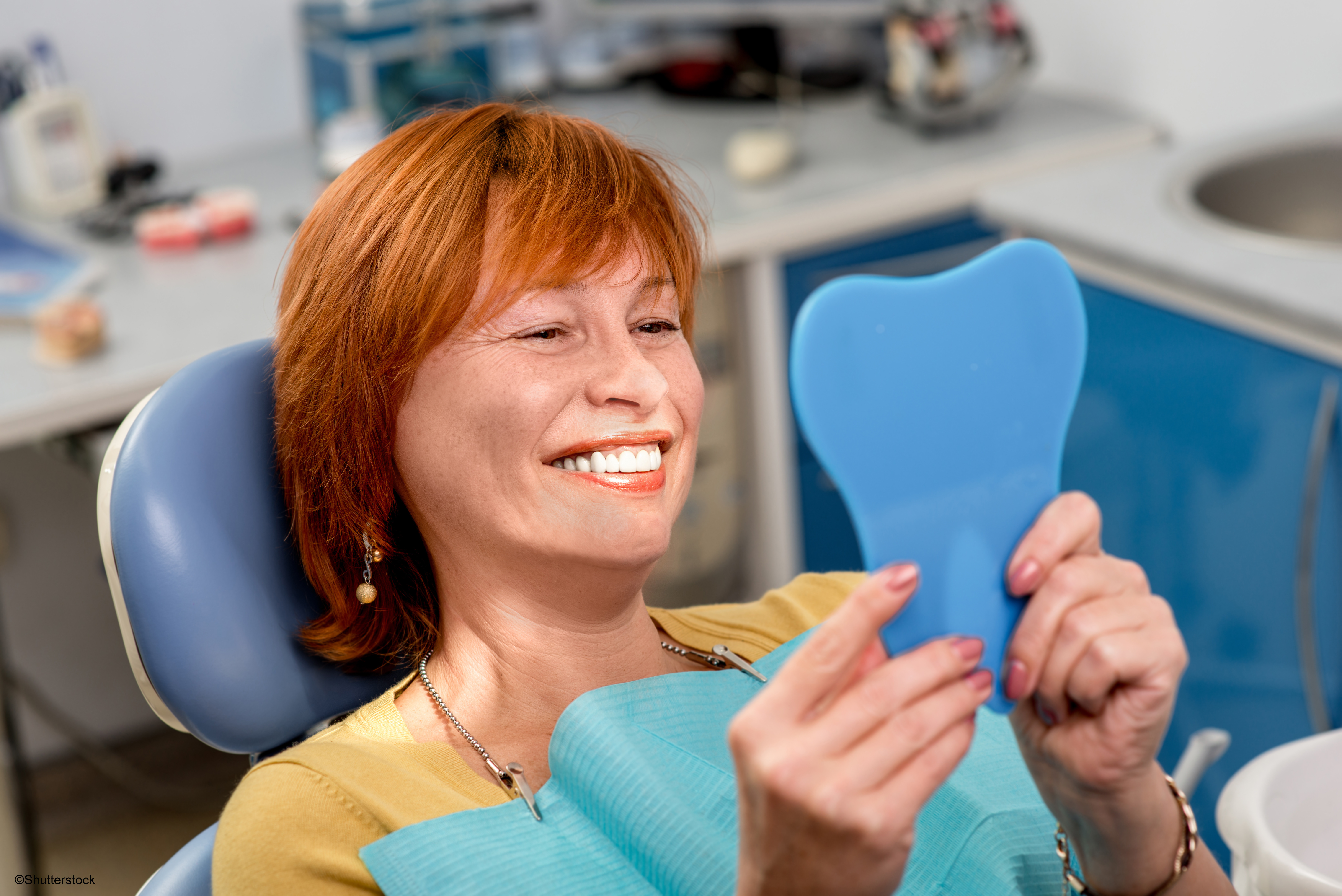 Woman sitting in dentist chair smiling into a mirror